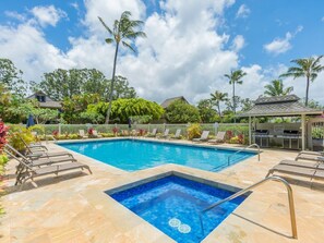 A rectangular swimming pool with a small hot tub section, surrounded by lounge chairs and a covered seating area.