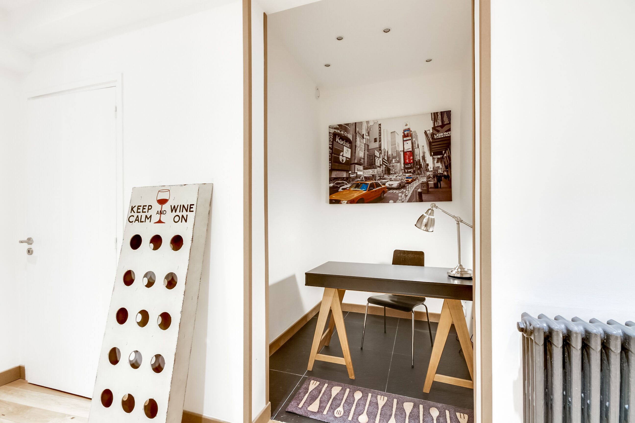 A room with a dining table, a chair, a radiator, and a wall-mounted picture of a cityscape.