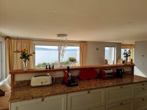 A kitchen with a view of a lake, equipped with a toaster, kettle, and red cups on the counter.