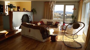 A cozy living room with a sofa, a chair, and a view of a mountainous landscape through large windows.