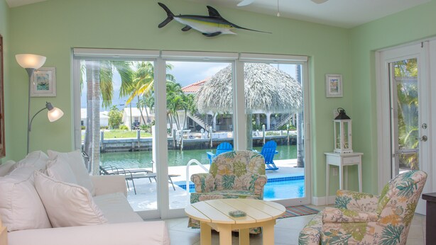 A room with a pool view, a ceiling fan, and a tropical-themed chair. - Flamingo Nook. Renovated, Private Pool, Canal & Cabana Club Access! (Key Colony Beach)