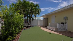 A backyard with artificial turf, a white fence, and a palm tree. - Flamingo Nook. Renovated, Private Pool, Canal & Cabana Club Access! (Key Colony Beach)
