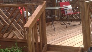 A wooden deck with a table and chairs, a hanging flower basket, and a brick building with windows. - Modern Home in The Center of it All -  Location, Location, Location!  (Nashville)