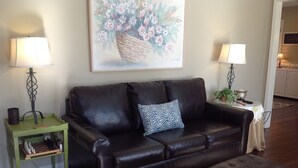 A living room with a black leather sofa, a patterned throw pillow, a chessboard, and a painting of flowers on the wall. - Modern Home in The Center of it All -  Location, Location, Location!  (Nashville)