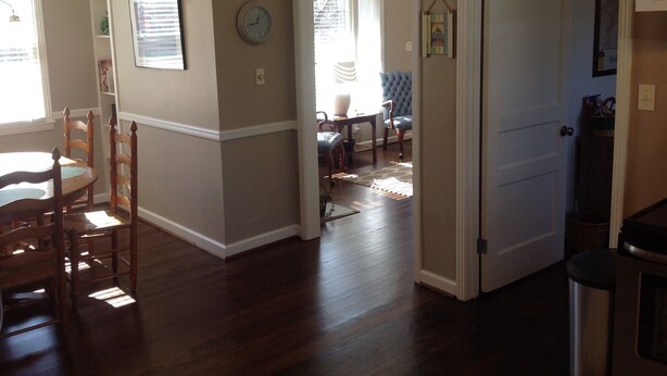A spacious room with hardwood floors, a dining area with wooden chairs, a blue upholstered chair, and a door leading to another room. - Modern Home in The Center of it All -  Location, Location, Location!  (Nashville)