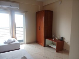 A hotel room with a bed, a wooden wardrobe, a small table with a kettle, and a window with curtains.