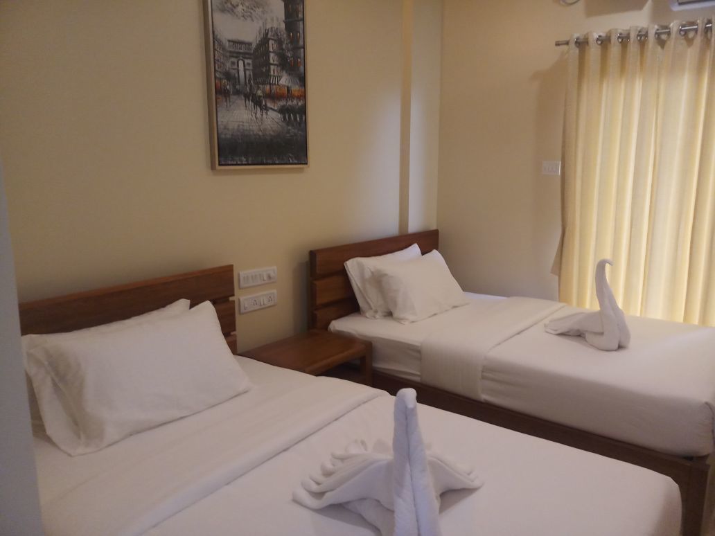 A hotel room with two beds, each with white linens and a swan-shaped towel on the bed. There is a painting on the wall and a curtain on the window.