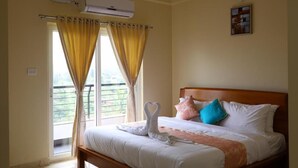 A bedroom with a bed, curtains, an air conditioning unit, and a painting on the wall. - Lali Petals (Madikeri)