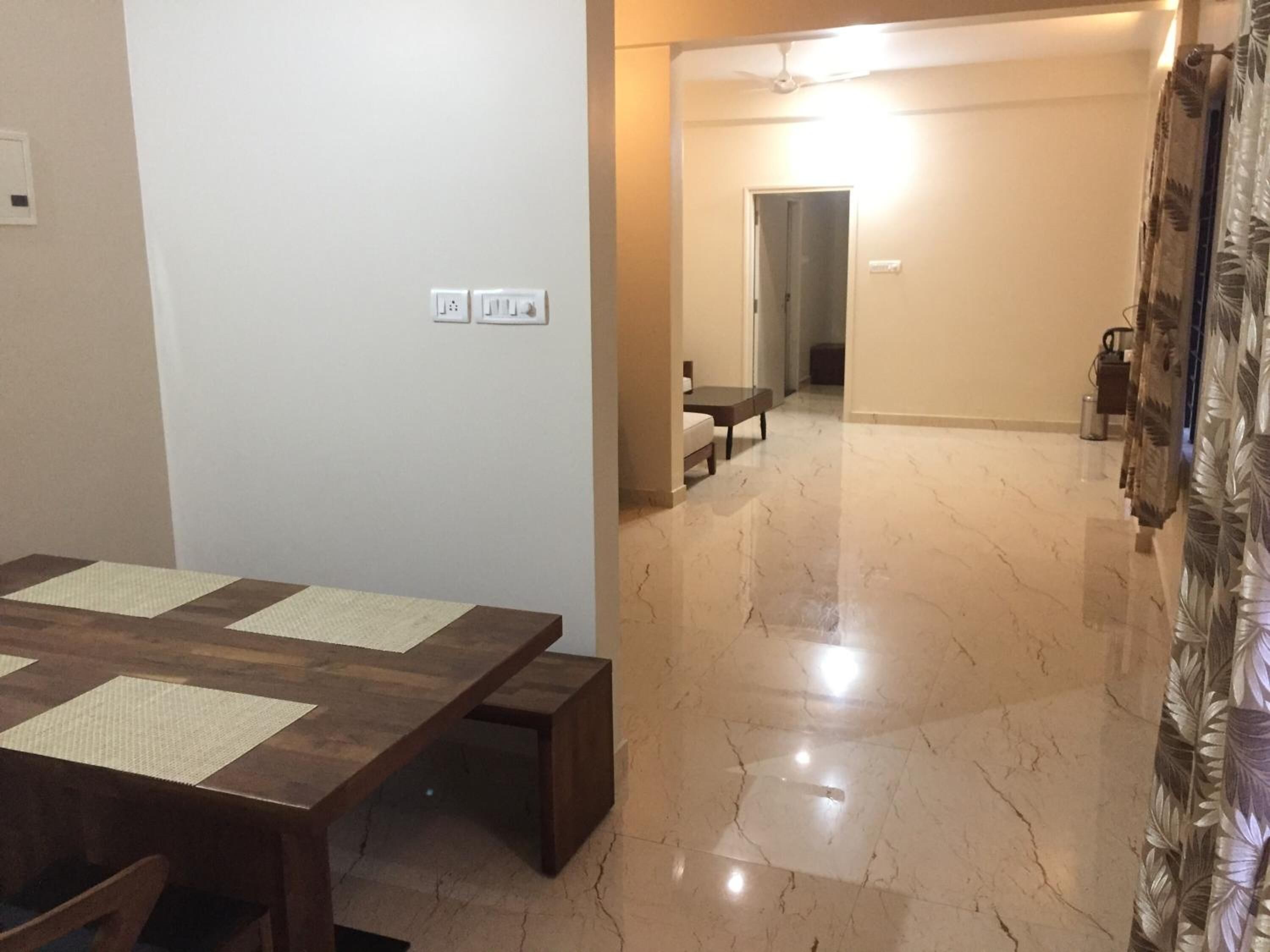 Uma área de refeições com mesa e bancos de madeira, um corredor com ventilador de teto e uma porta que dá para outro cômodo.