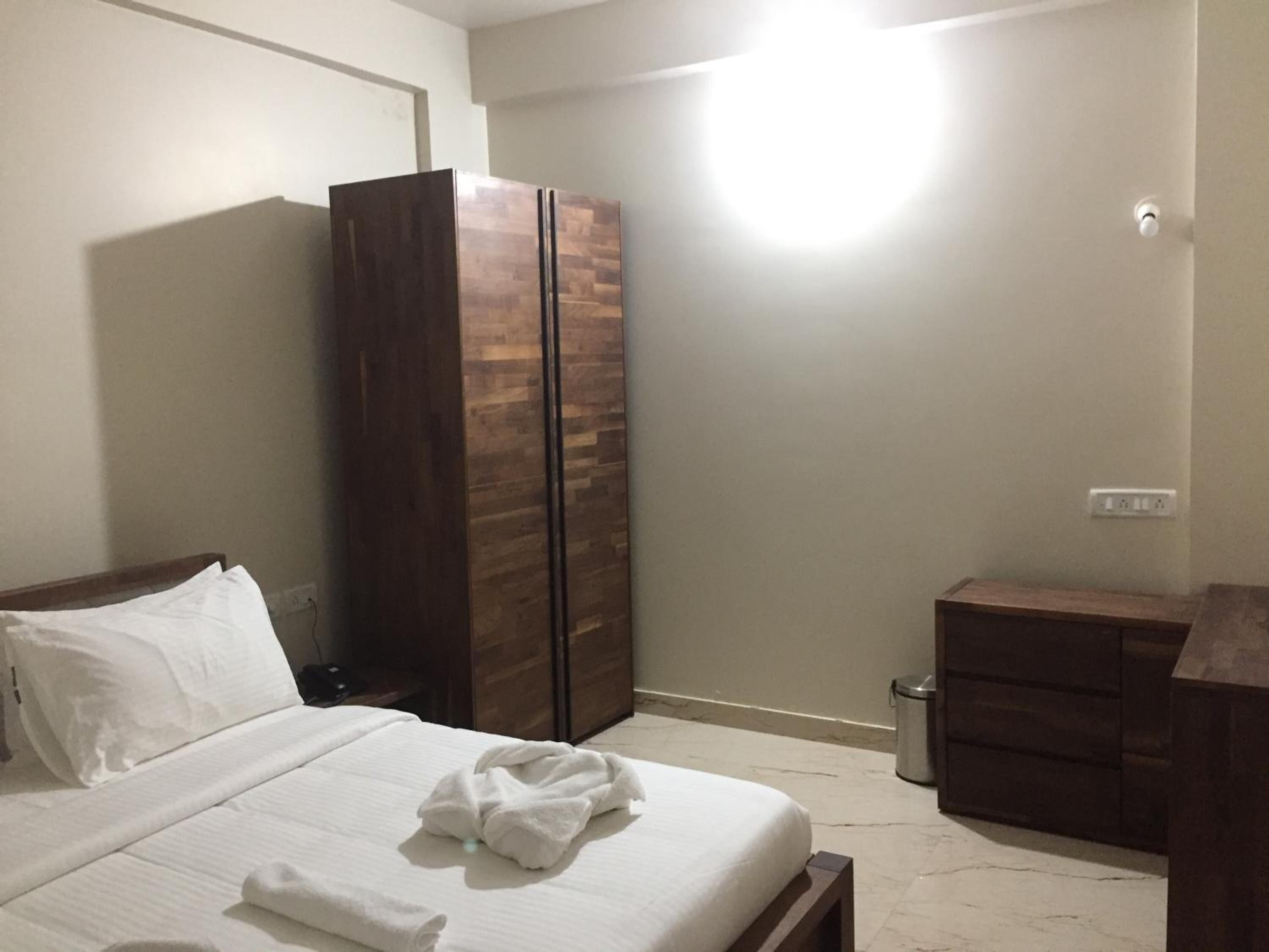 A bedroom with a bed, a wardrobe, a bedside table, and a trash bin.