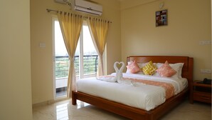A bedroom with a bed, curtains, an air conditioning unit, a bedside table, and a view through the window. - Lali Petals (Madikeri)