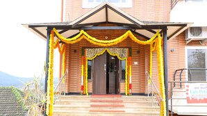 A building entrance with a covered porch decorated with yellow and orange flowers, a staircase leading up to the door, and a signboard on the right. - Lali Petals (Madikeri)