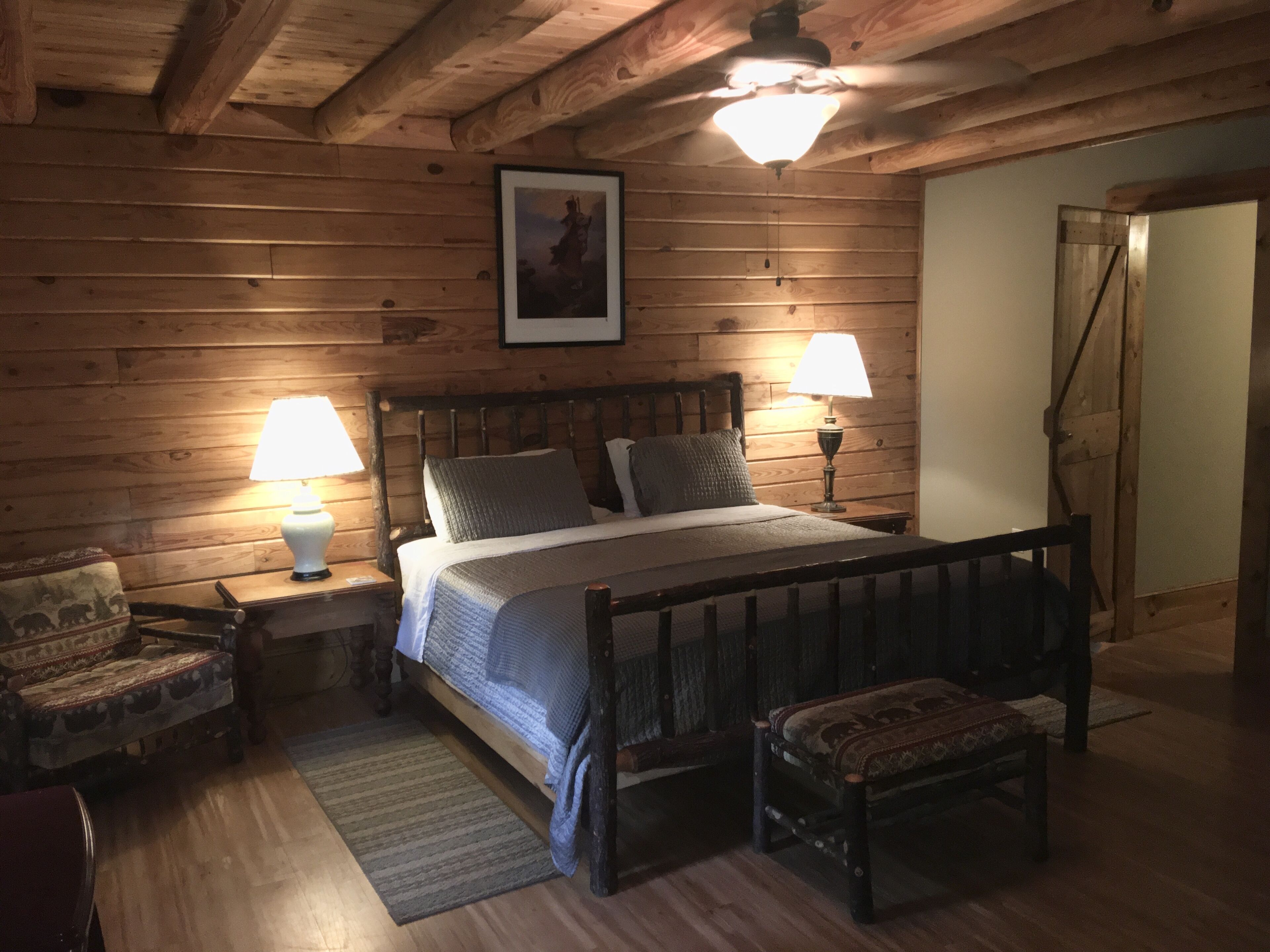 Un dormitorio con paneles de madera, una cama, dos lámparas de noche, una silla y un banco.