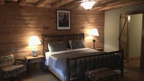 Un dormitorio con paneles de madera, una cama, dos lámparas de noche, una silla y un banco.