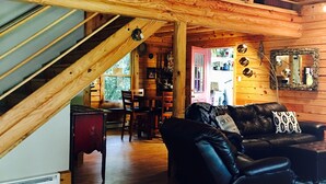 Amplia sala de estar con una escalera de madera, un sofá de cuero y un comedor con sillas y una mesa.