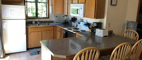 A kitchen with wooden cabinets, a central island with bar stools, a refrigerator, a sink, a microwave, and a stove.