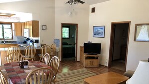 Uma sala de estar com área de jantar, uma televisão em um suporte de madeira e uma cozinha ao fundo.