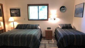 Quarto com duas camas, mesa de cabeceira com relógio, janela com persianas e decoração na parede.