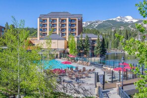 Un albergo con area piscina, immerso tra alberi e con vista su una montagna.