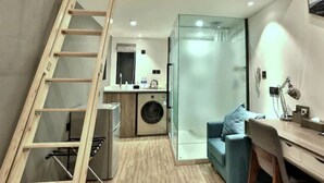 Un espacio habitable compacto con dormitorio en entrepiso, lavadora, escritorio y una silla.