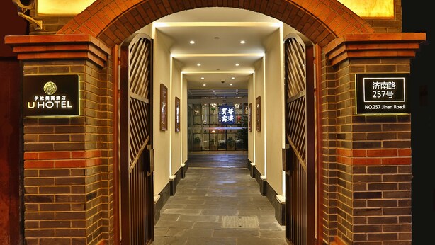 Entrada de hotel con un arco de ladrillo, una señal con el nombre del hotel y una señal con la dirección.
