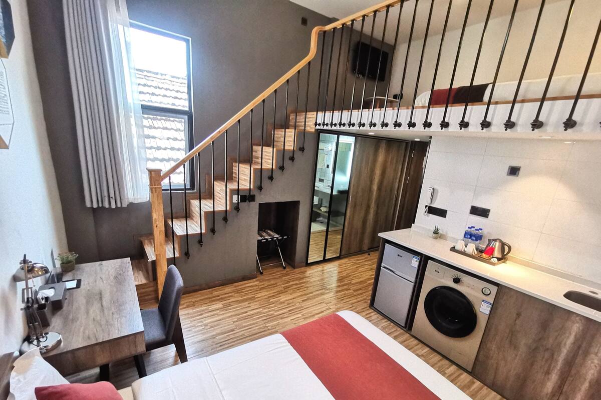 Una habitación de hotel compacta con cama, un escritorio pequeño, lavadora y kitchenette.