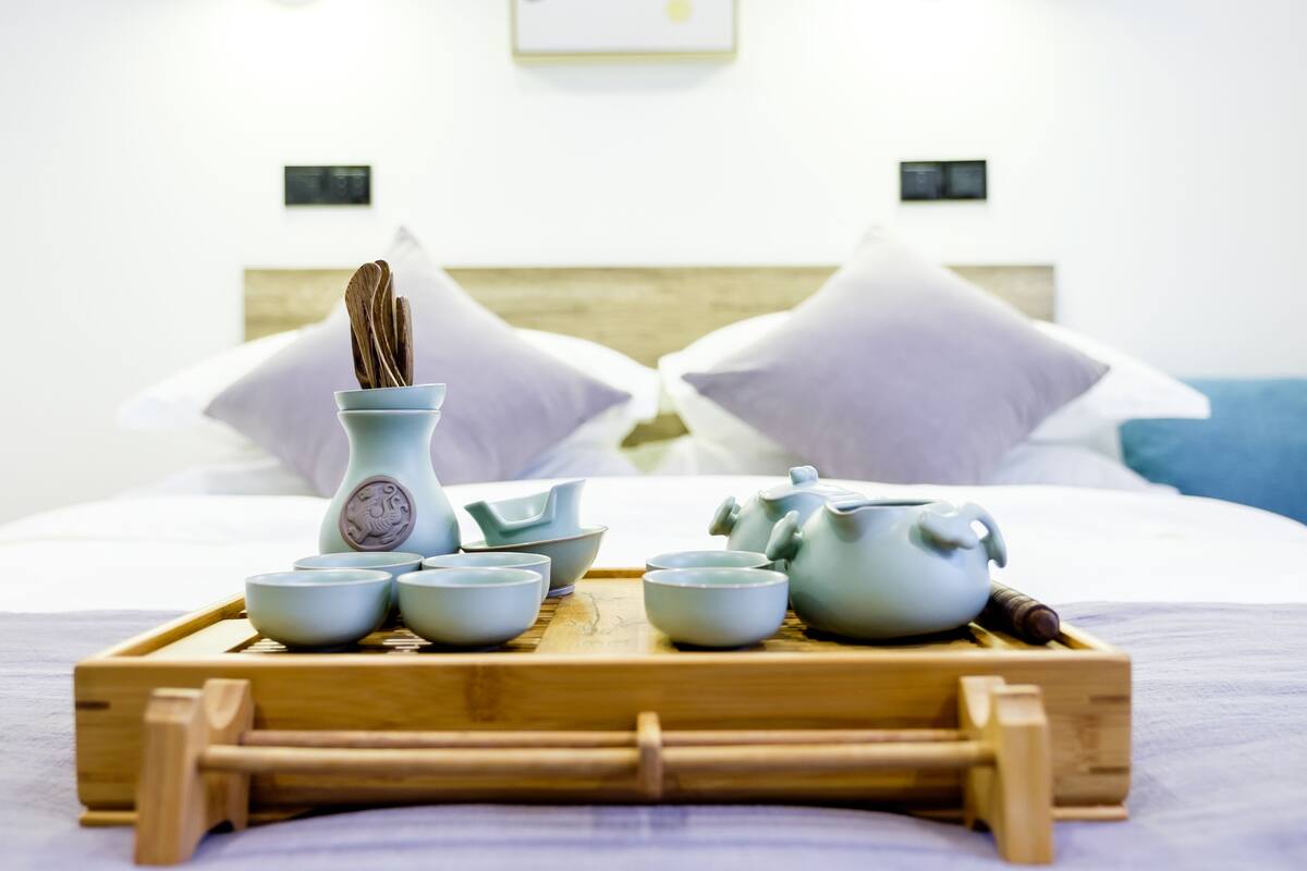 Un juego de té ordenado sobre una bandeja en una habitación de hotel, con una cama y almohadas al fondo.