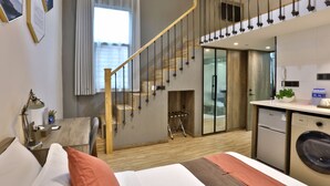 Una habitación de hotel moderna con una escalera de madera, una cama con almohadas, un escritorio con lámpara y una lavadora.