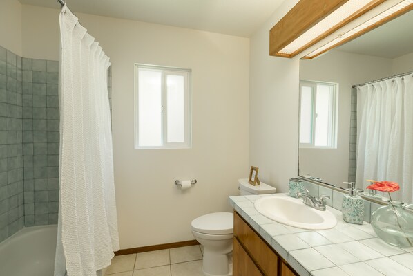 A bathroom with a white toilet, a sink, a shower with a white curtain, and a mirror above the sink.