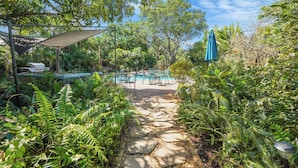 Un chemin de pierre mène à un espace piscine agrémenté d’un coin salon extérieur et d’un barbecue.
