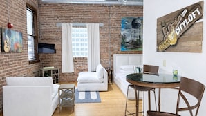 Una sala de estar moderna con una pared de ladrillo, muebles blancos, una mesa de vidrio y un cuadro de una guitarra.