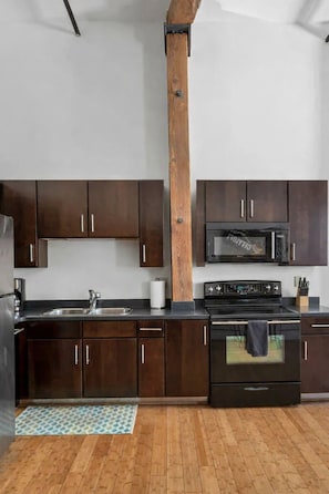 A modern kitchen with dark wooden cabinets, a stainless steel sink, a microwave, and a stove.