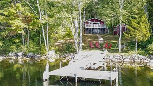 A dock extending into a lake with a house and a shed in the background.