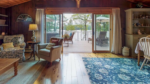 A cozy room with wooden floors, a blue patterned rug, a sofa, a chair, a lamp, and a bookshelf.