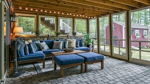 A covered porch with a blue sofa, wooden coffee table, and a fan.