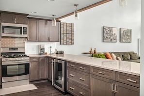 A modern kitchen with dark wood cabinets, stainless steel appliances, a granite countertop, and a dining area with a sofa and cushions.