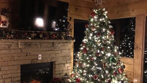 Ein gemütliches Zimmer mit Kamin, Weihnachtsbaum und Wandfernseher.