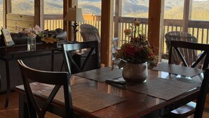 Eine Holzterrasse mit Tisch und Stühlen, einem Blumenstrauß und Blick auf Berge.