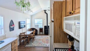 A compact kitchen with wooden cabinets, a stove, and a microwave. There is a dining area with a table and chairs, and a chandelier hanging from the ceiling. - Cozy Private Beach Bungalow, New Hot Tub,  1 Dog ok, 3 short Blocks To Beach. (Santa Cruz)