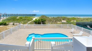 A swimming pool with a view of the beach and a pier in the background.