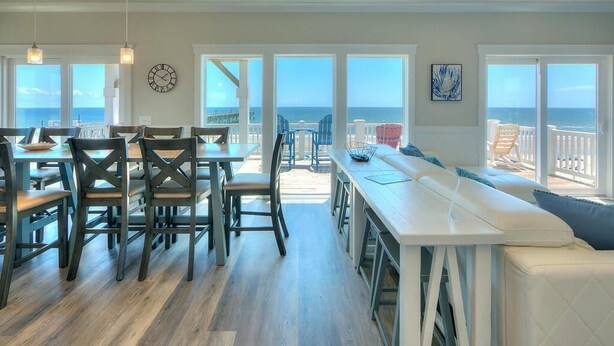 A spacious dining area with a view of the ocean, a large white sofa, and a dining table with chairs.