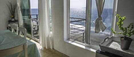 A balcony with a view of the sea, a dining area with a table and chairs, and a potted plant on the windowsill.