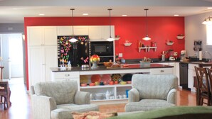 A modern kitchen with white cabinets, a black refrigerator, and a red accent wall. There are two chairs in the living area with a green couch. - Stay in downtown Three Oaks overlooking the main street!  (Three Oaks)