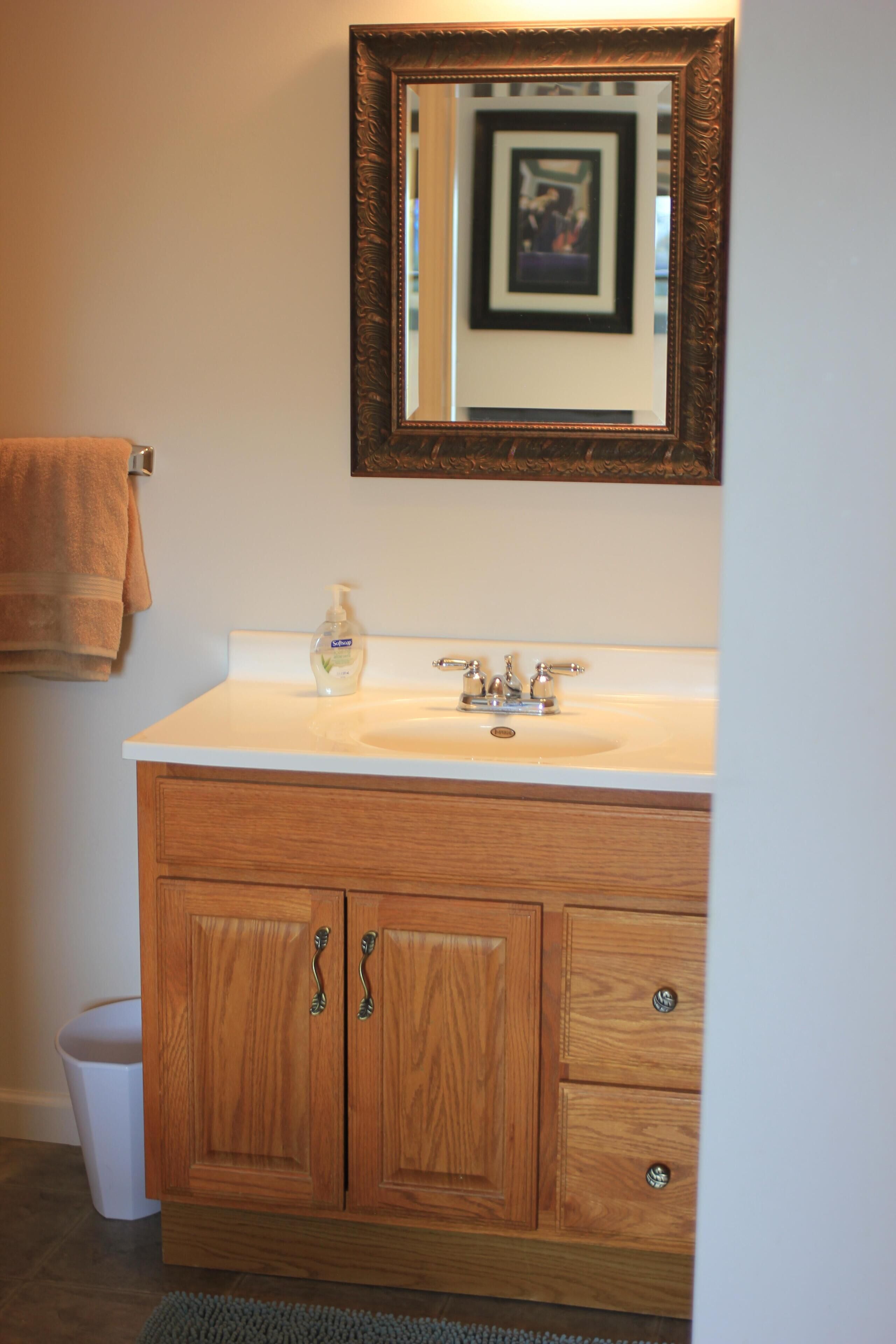 A bathroom with a wooden vanity, a sink, a mirror, and a towel hanging on the wall.
