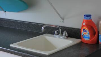 Eine Spüle mit Arbeitsplatte, eine Tide-Flasche und ein Regal mit Küchenpapier und anderen Gegenständen.