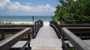 A wooden boardwalk leading to a beach with a clear view of the ocean and a signpost.