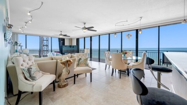 A spacious living area with a balcony overlooking the sea, furnished with sofas and chairs, and a dining table.