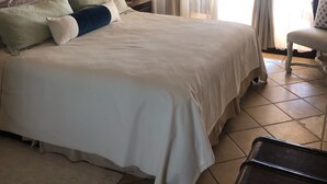 Uma cama bem arrumada com cabeceira, uma mesa de cabeceira com abajur e uma cadeira.