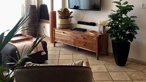 Uma sala de estar com televisão de tela plana na parede, um armário de madeira, uma planta grande em vaso e um espelho.