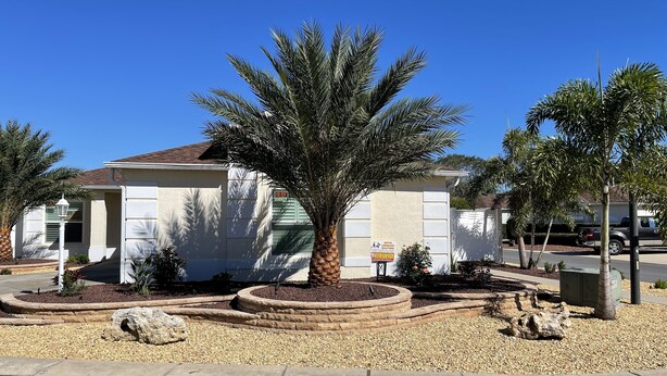 A single-story house with a 'For Rent' sign, surrounded by landscaped gardens and a palm tree. - Beautifully Refurbished villa in an exciting active retirement community. (The Villages)